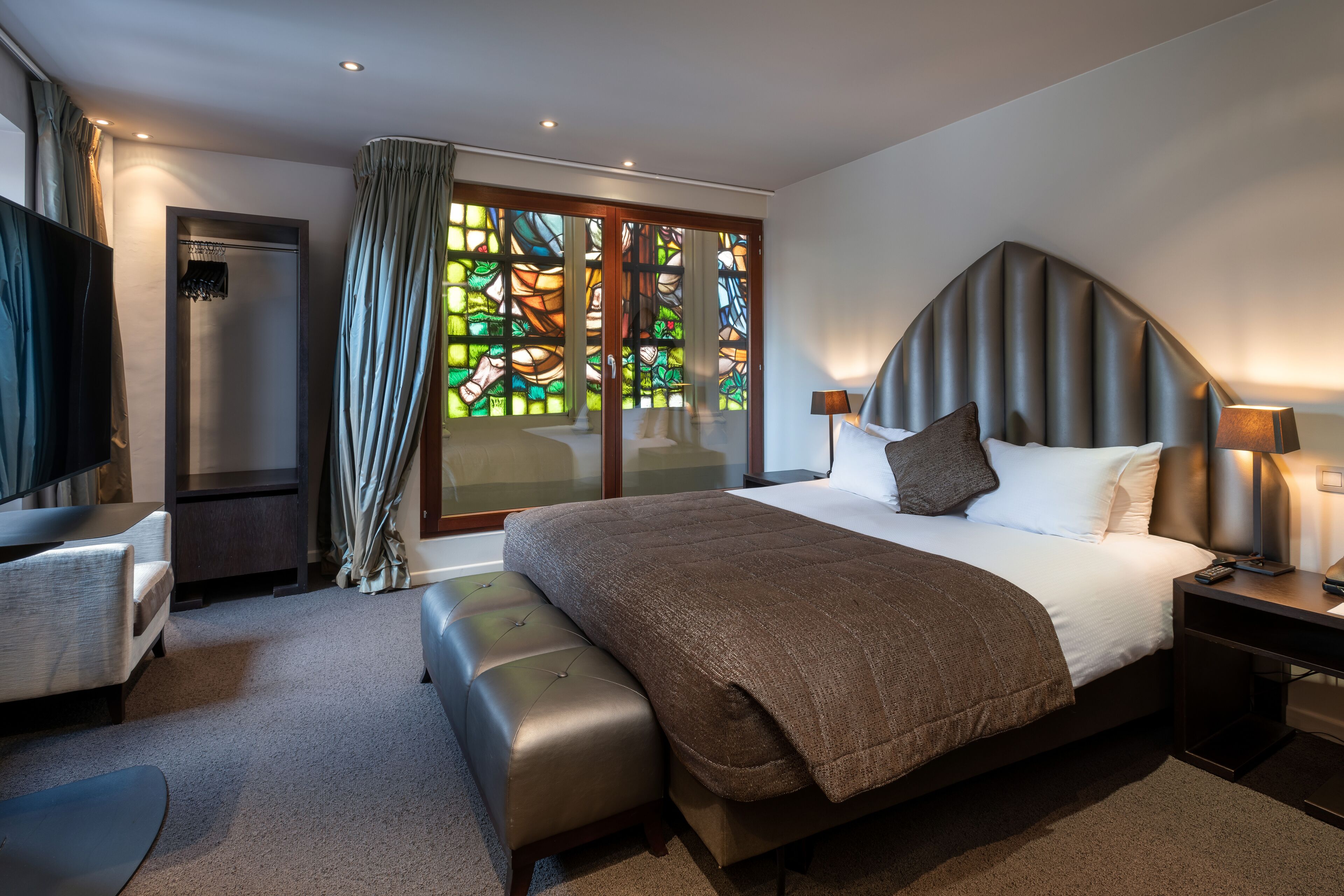 A modern hotel room with a large bed, a TV, a desk, and a shower area.