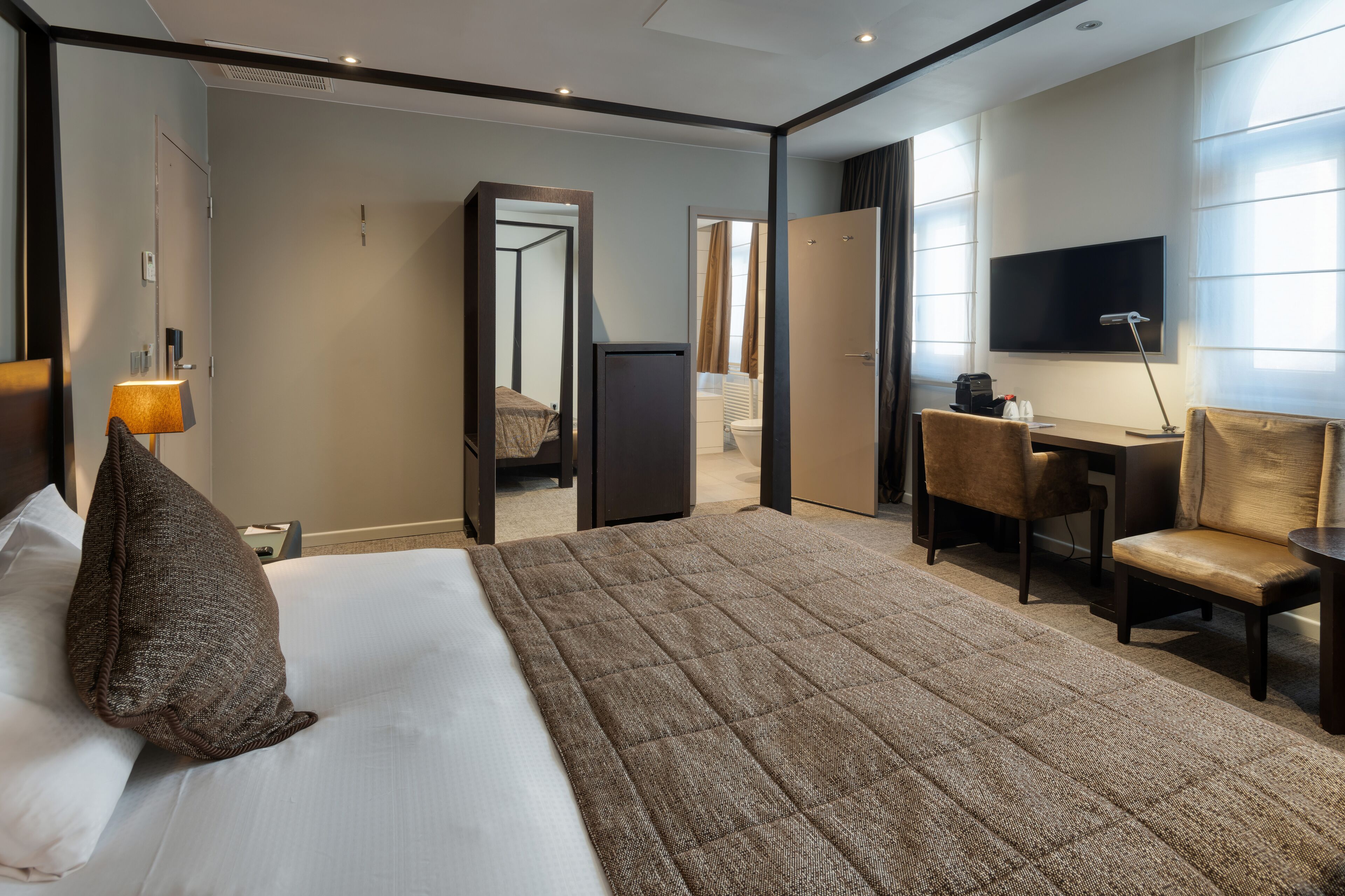 Una habitación de hotel con cama, escritorio, silla, televisor y espejo.