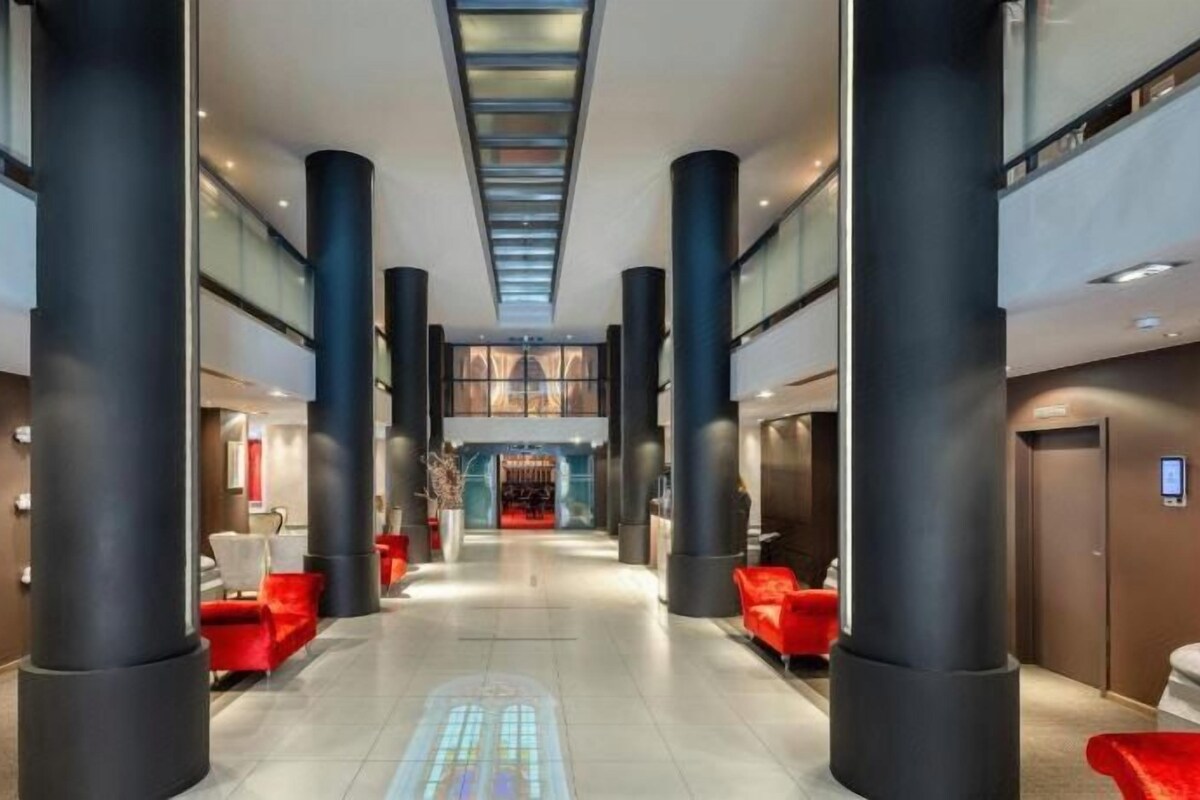 Un vestíbulo de hotel con un espacio central abierto, grandes columnas negras y zonas de estar rojas.
