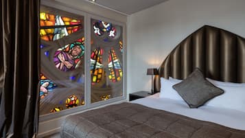Quarto com uma cama grande, cabeceira, mesa de cabeceira e janela de vitrais.