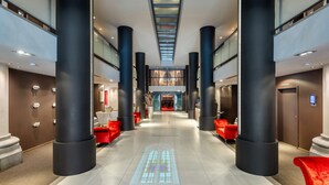 A spacious hotel lobby with a central corridor, large pillars, and red seating areas. - Martin's Patershof (Mechelen)