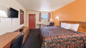 Ein Hotelzimmer mit Bett, Schreibtisch, Stuhl, Fernseher, einem Fenster mit Vorhängen und einer Lampe.