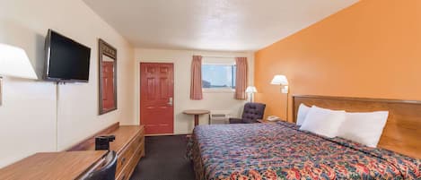 Une chambre d’hôtel avec un lit, un bureau, une chaise, une télévision, une fenêtre avec des rideaux et une lampe.