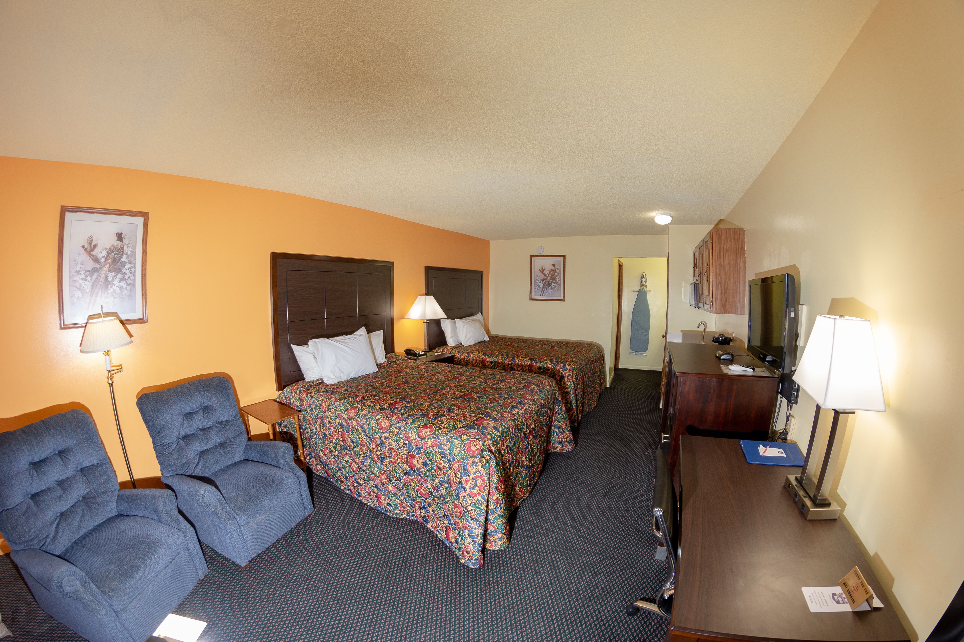 A hotel room with two beds, a desk, a chair, and a dresser.