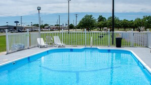 Ein Swimmingpool mit weißem Zaun, Liegestühlen und einem Mülleimer.