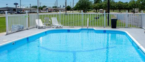 A swimming pool with a white fence, lounge chairs, and a trash can.