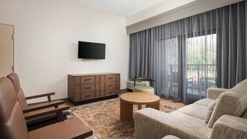 Una sala de estar moderna con un sofá, una mesa de centro, un televisor montado en la pared, un mueble pequeño y un ventanal con cortinas.