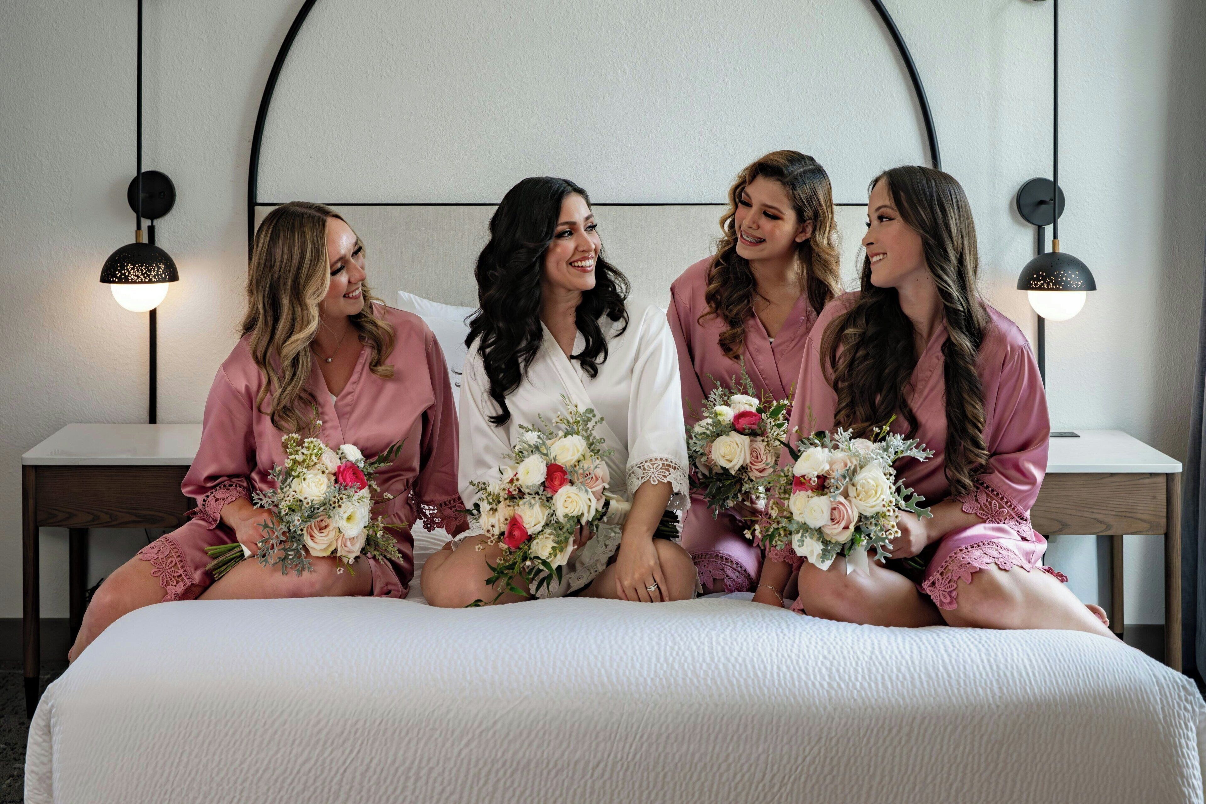 Un groupe de quatre personnes est assis sur un lit doté d’une tête de lit blanche et tient des bouquets de fleurs.
