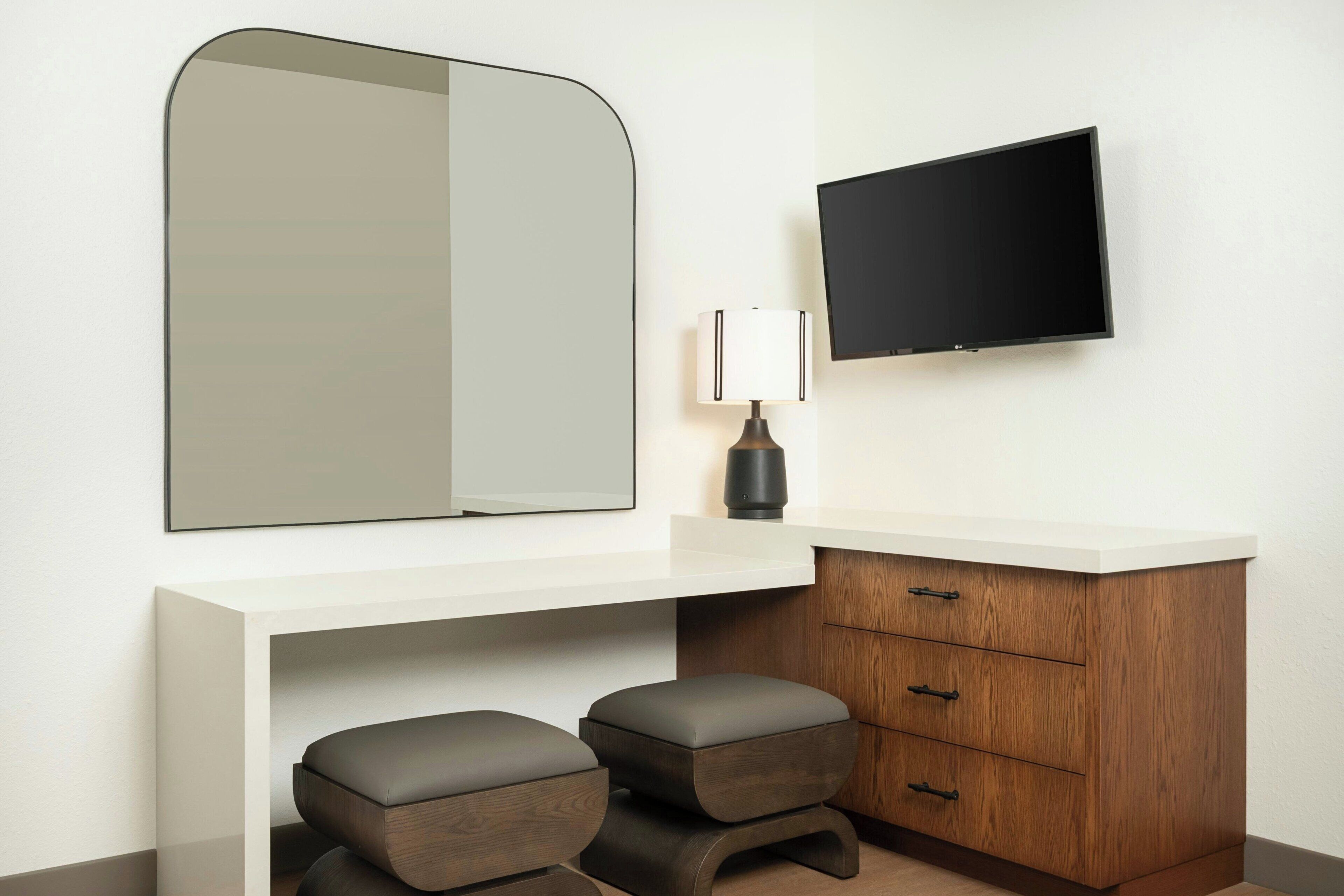 Une salle de bain moderne avec un grand miroir, un téléviseur à écran plat, un meuble-lavabo en bois doté de tiroirs et deux tabourets.