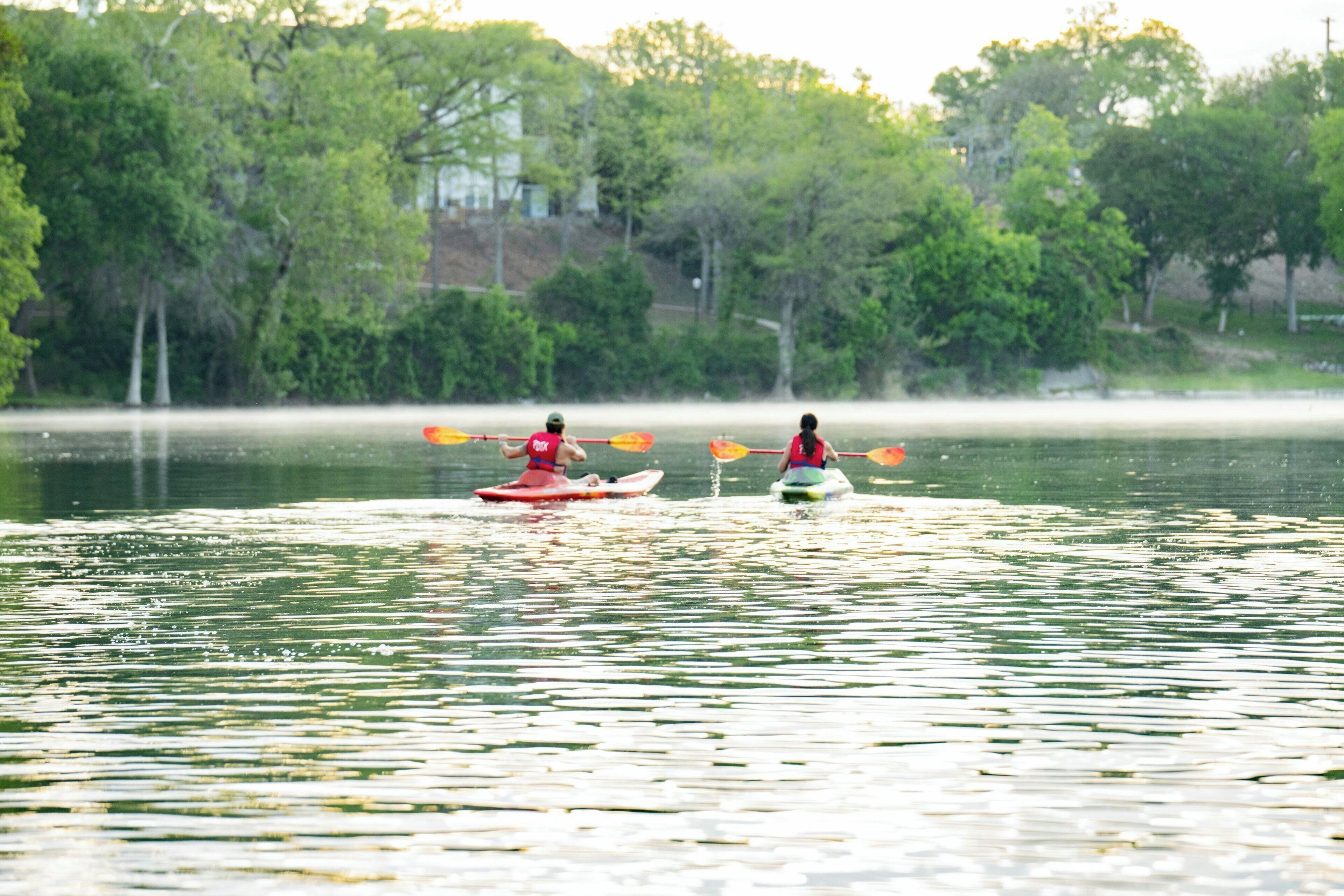 Two kayakers on a calm lake with trees in the background.