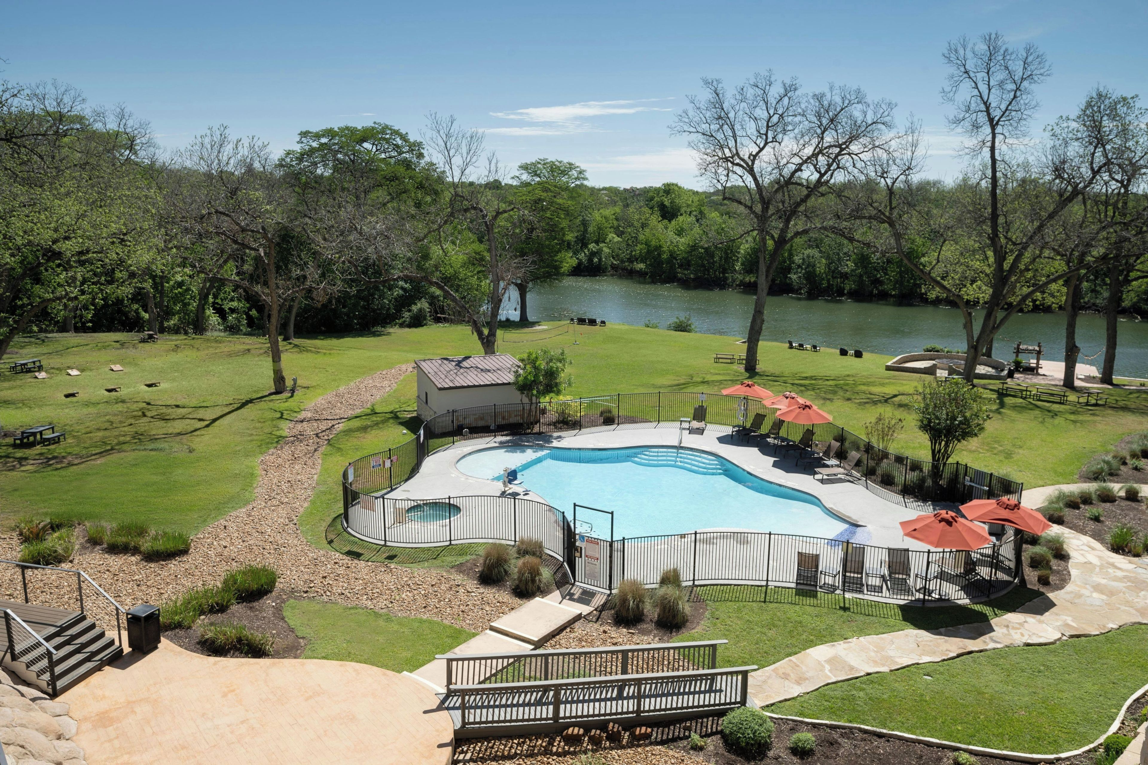 A swimming pool with a deck, surrounded by a fence, with a lake in the background.