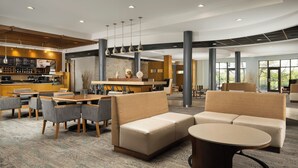 Un moderno vestíbulo de hotel con zonas de estar, un bar y grandes ventanales.