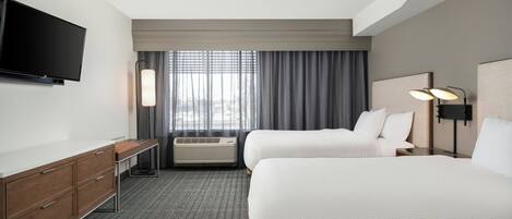 A hotel room with two beds, a TV, a desk, and a window with curtains.