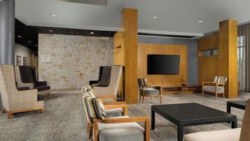 A modern lobby with stone walls, wooden furniture, a flat-screen TV, and a carpeted floor.