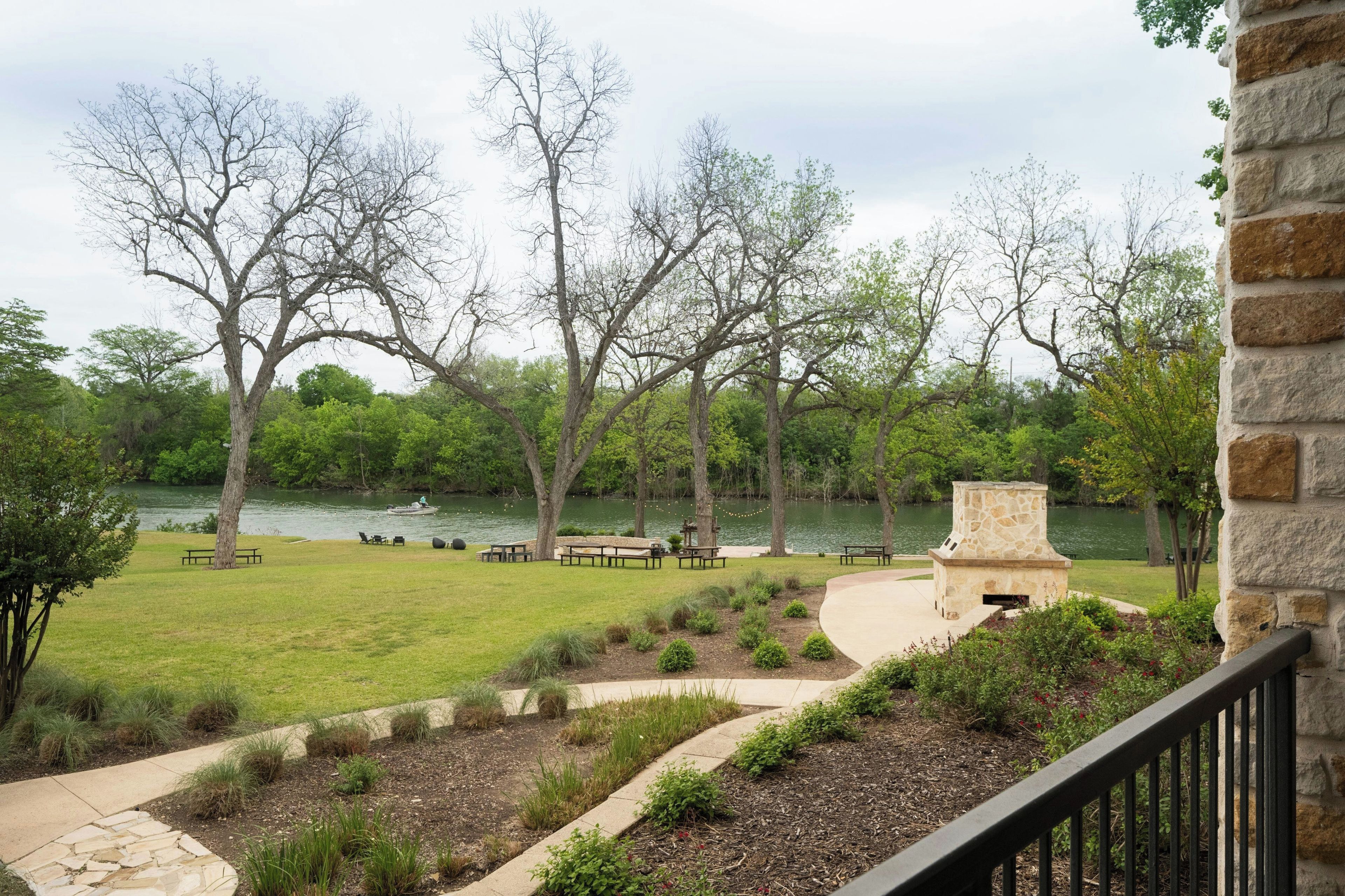 A lakeside outdoor area with picnic tables and a stone fireplace.