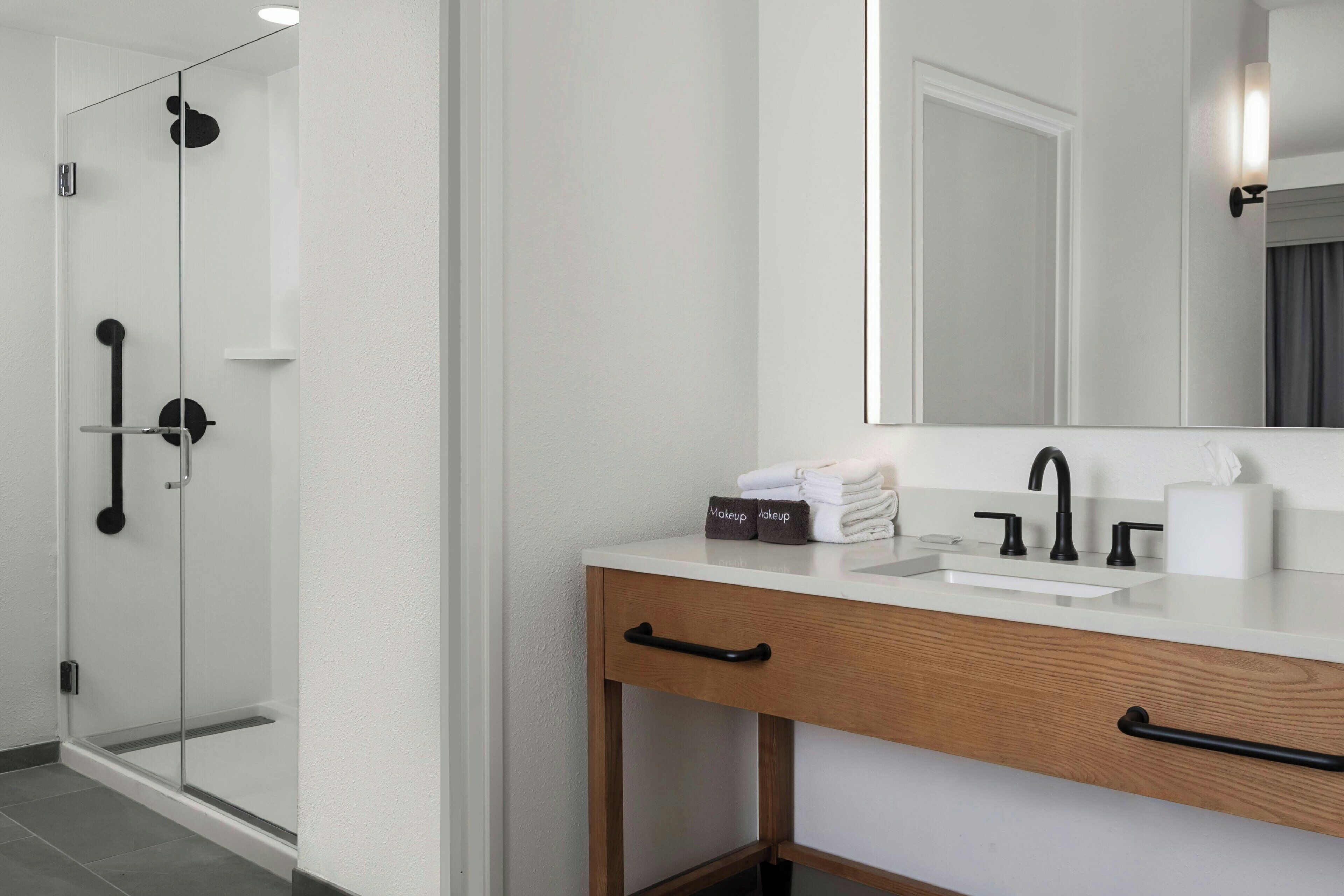 A modern bathroom with a glass shower enclosure, a white sink with a black faucet, and a wooden vanity with a mirror.