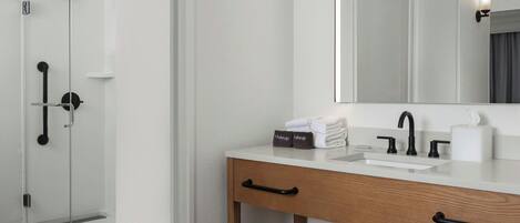 A modern bathroom with a glass shower enclosure, a white sink with a black faucet, and a wooden vanity with a mirror.