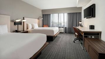A hotel room with two beds, a desk, a chair, a TV, and a window with curtains.