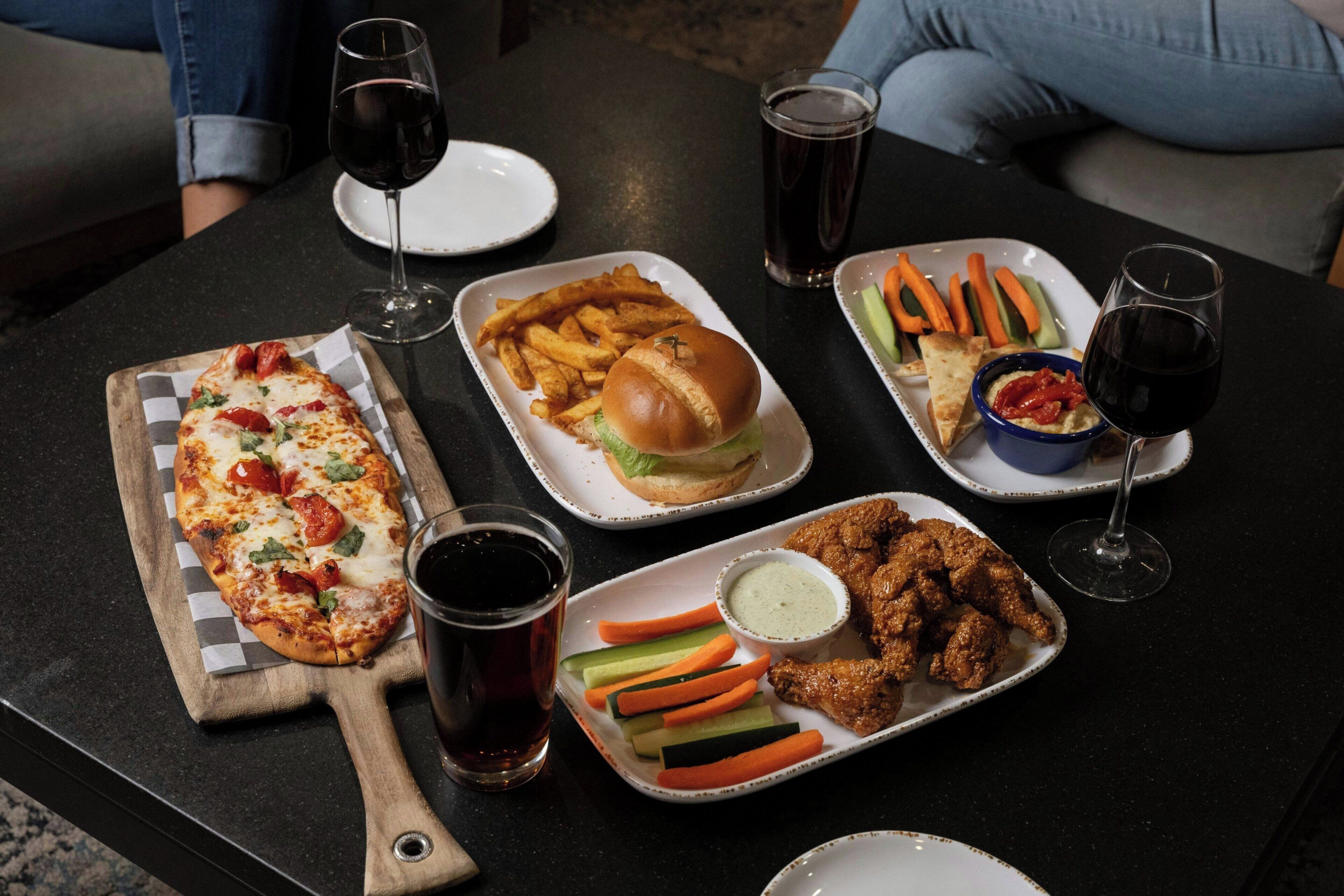A table with a pizza, burger, fries, chicken wings, and various sides.