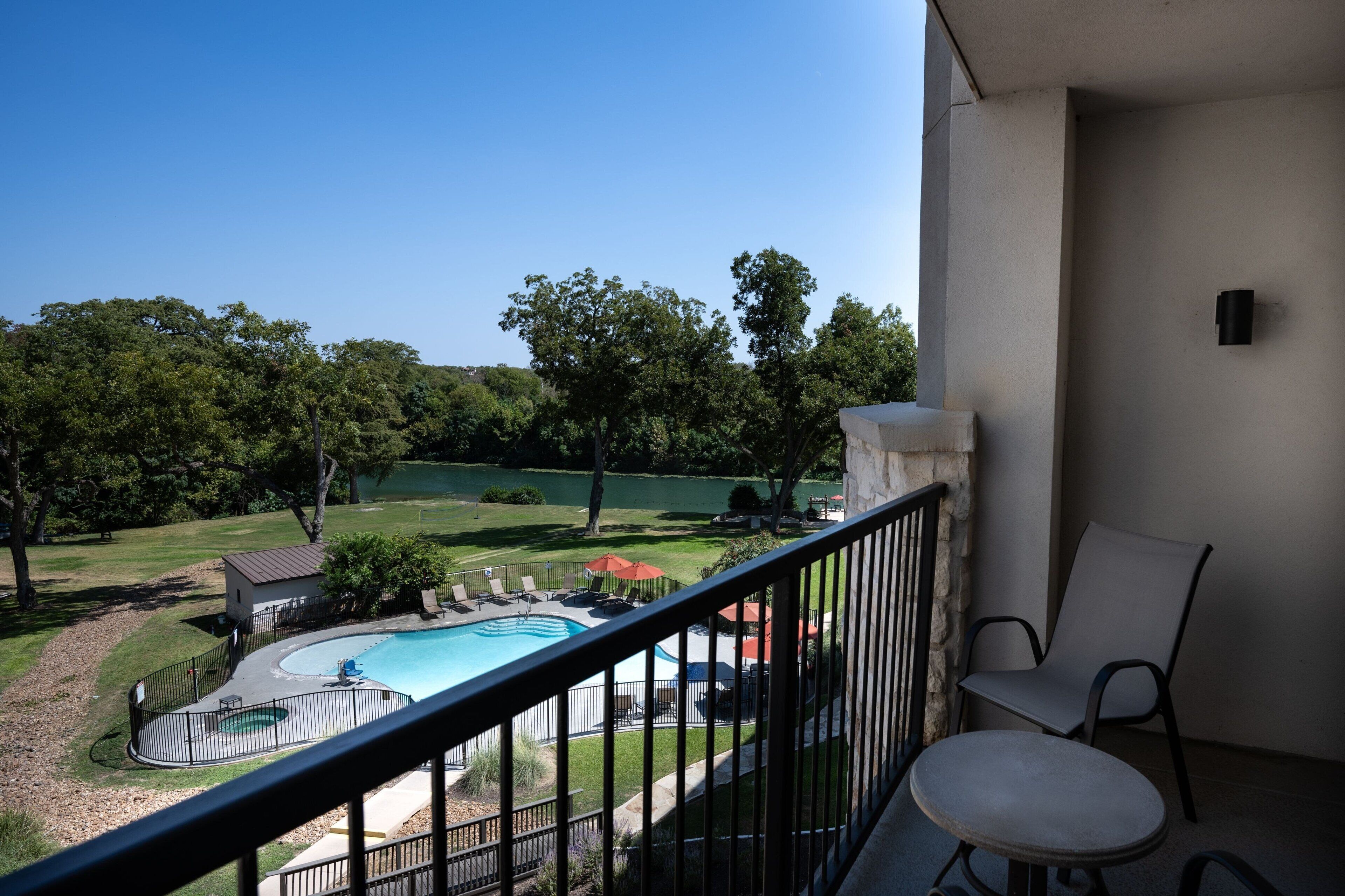 Un balcón con vistas a una piscina, un césped y un edificio pequeño.