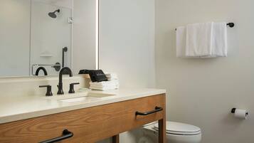 Un baño con lavamanos blanco, grifo negro, tocador de madera, espejo, toallero y retrete.