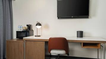 A hotel room with a desk, a chair, a TV, a lamp, a microwave, and a minibar.