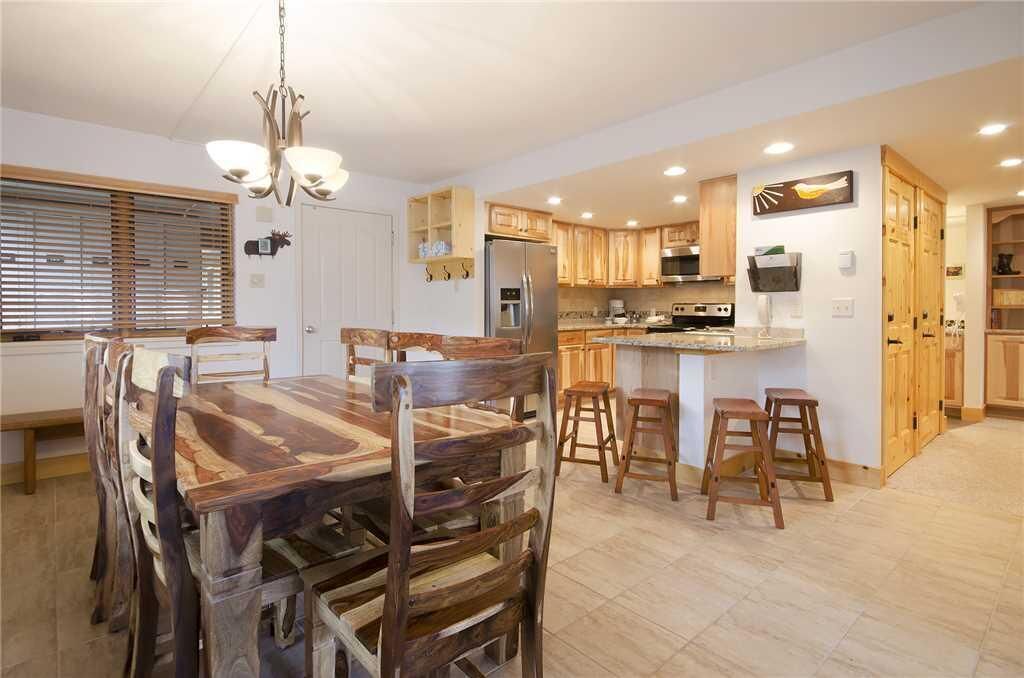 Una cocina moderna con armarios de madera, una isla central y una zona de comedor con mesa y sillas de madera.