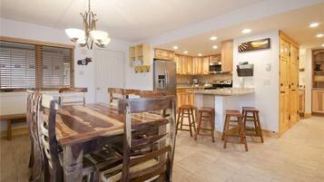 Una cocina moderna con armarios de madera, una isla central y una zona de comedor con mesa y sillas de madera.
