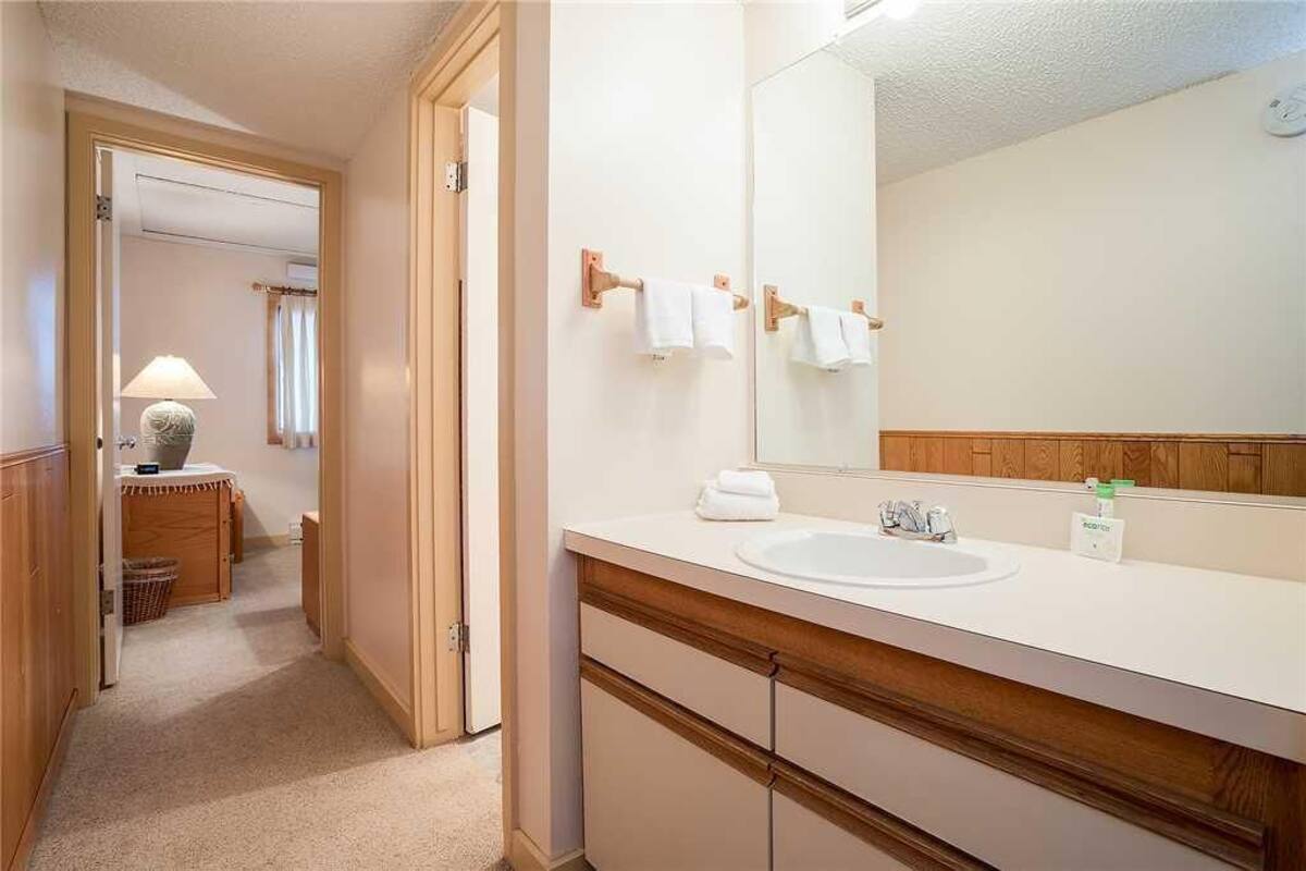 Une salle de bain d’hôtel avec un lavabo blanc, un meuble-lavabo en bois, un miroir et un porte-serviettes.