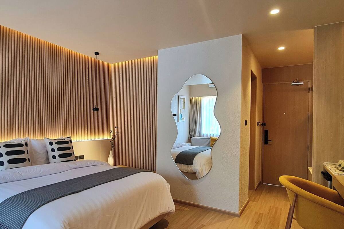 A modern hotel room with a large bed, a mirror, and a wooden panel wall.
