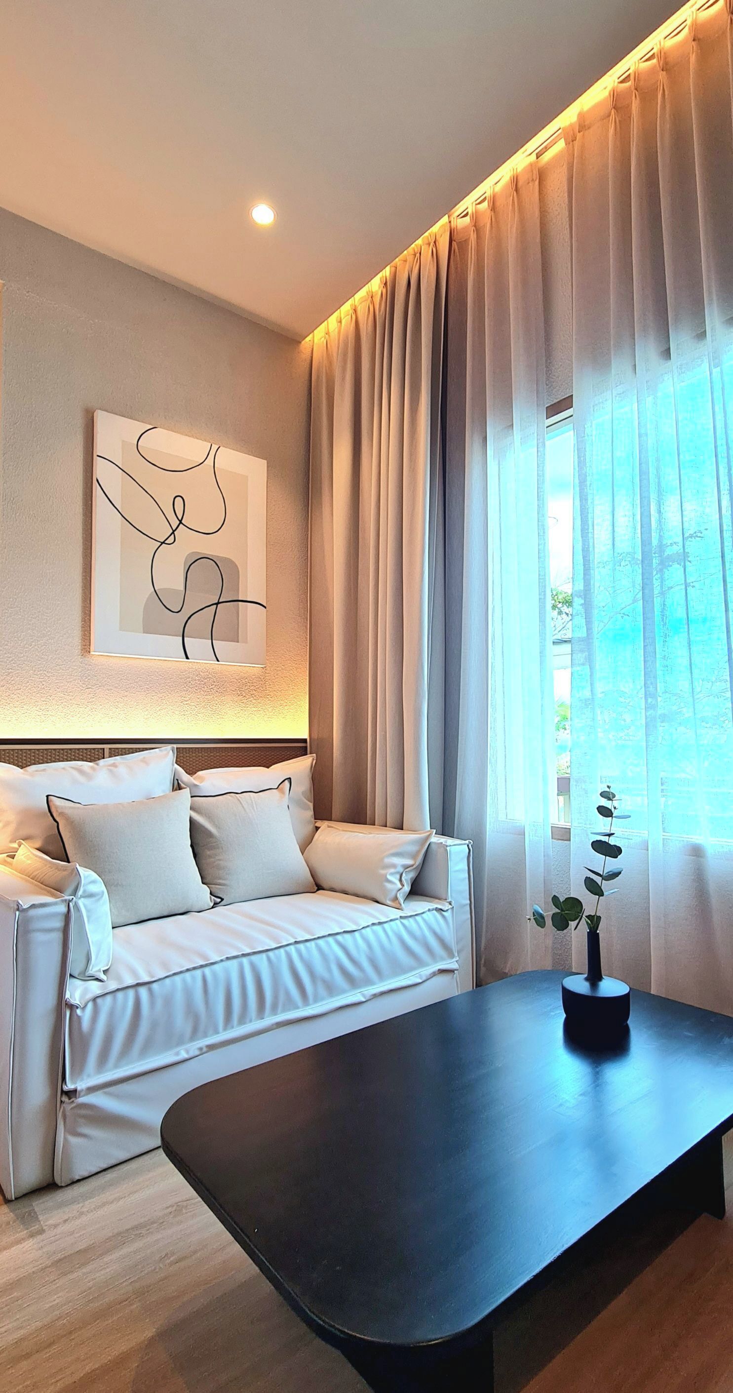 A modern living room with a sofa, a coffee table, a wall-mounted abstract art piece, and a window with curtains.