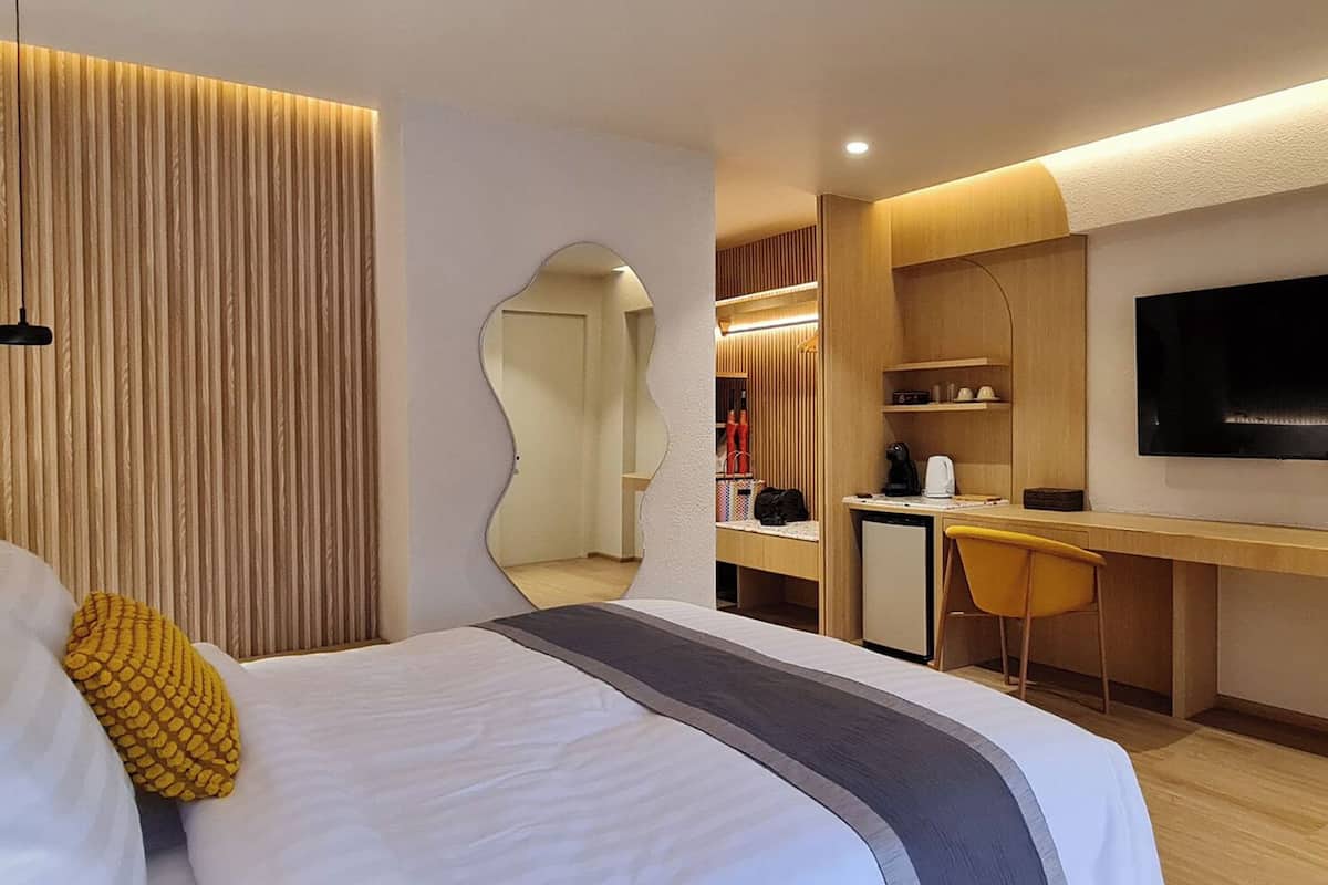A modern hotel room with a bed, a desk, a chair, and a TV.