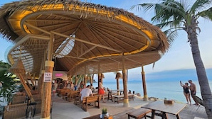 Un restaurante frente al mar con techo de paja y mesas y bancos de madera.