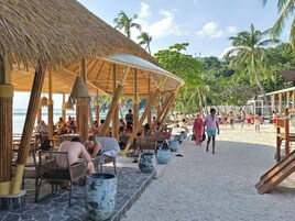 Un restaurante frente a la playa con terraza, palmeras y vistas al océano.