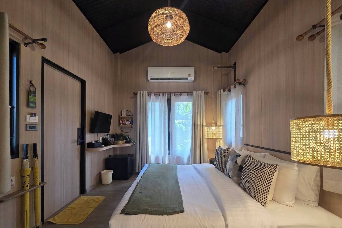 A hotel room with a bed, a television, an air conditioning unit, and a window with curtains.