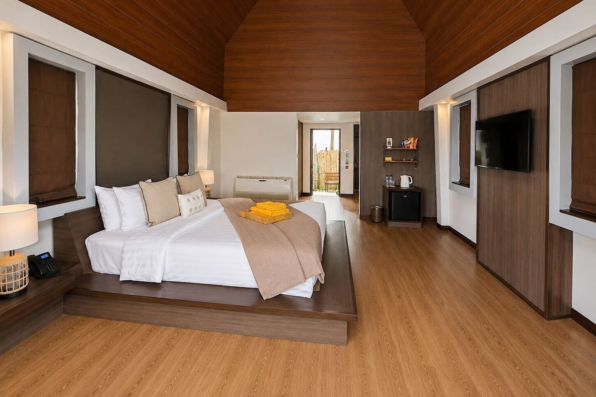 A modern hotel room with a large bed, a television, and a small kitchenette.