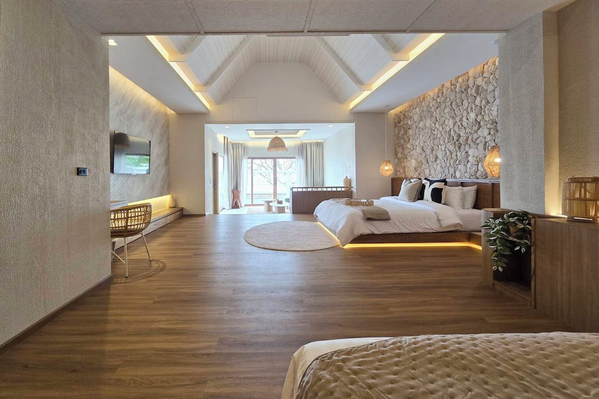 A spacious bedroom with a large bed, a seating area with a TV, and a stone wall.