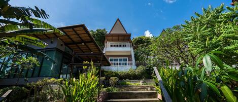 A staircase leading to a building with a triangular roof, surrounded by lush greenery.