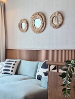Un salón moderno con un sofá azul claro, cojines estampados y tres espejos con marco rústico fijados a la pared.