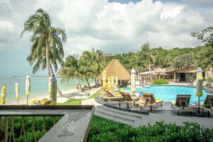 Un resort con piscina, sillas de descanso, sombrillas y palmeras.
