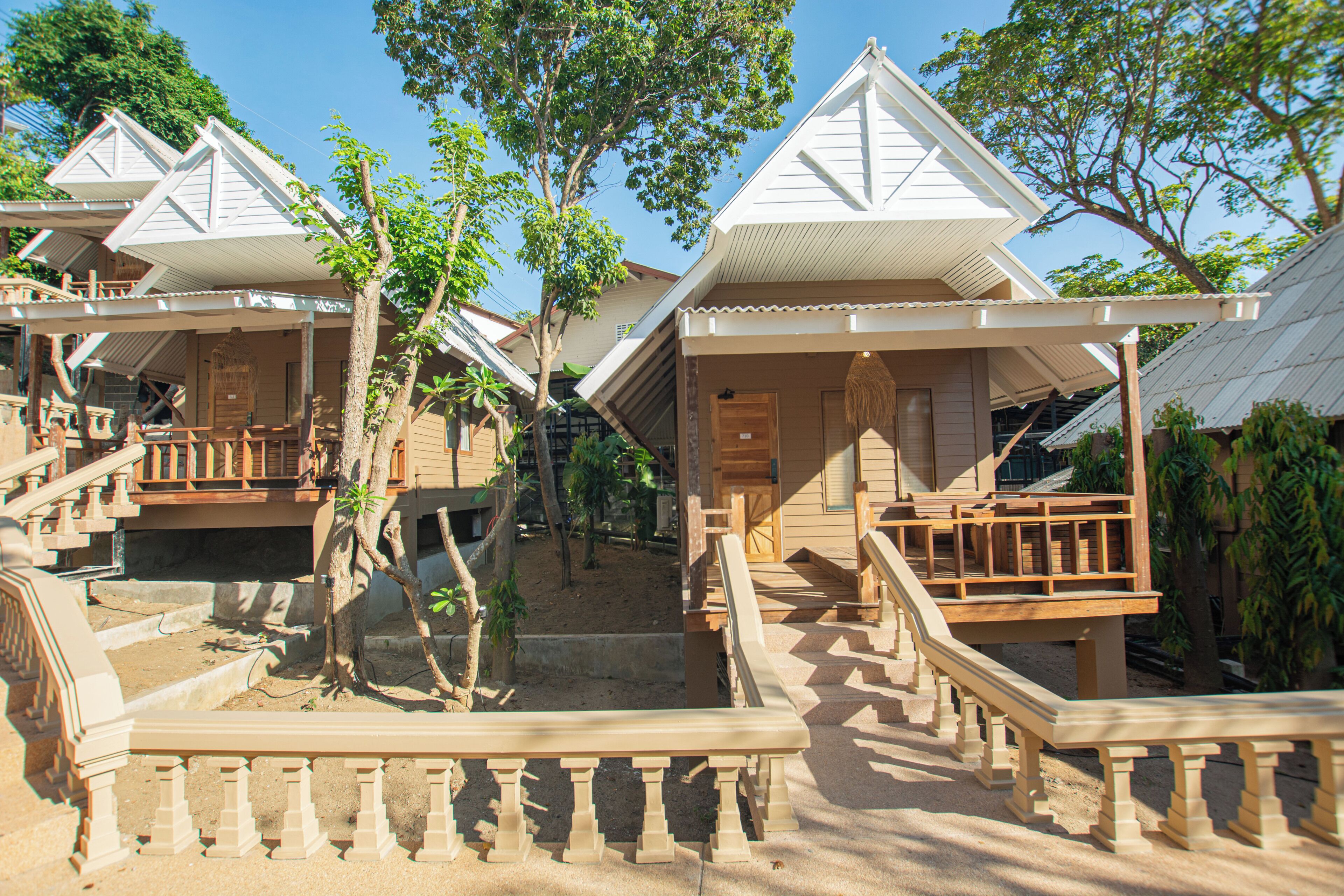 A row of wooden bungalows with balconies, a central staircase, and surrounding trees.