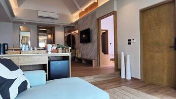 Una sala moderna con un sofá azul claro, una mesita de centro pequeña y un televisor montado en la pared. Se ve una puerta de madera y una zona de cocina al fondo.