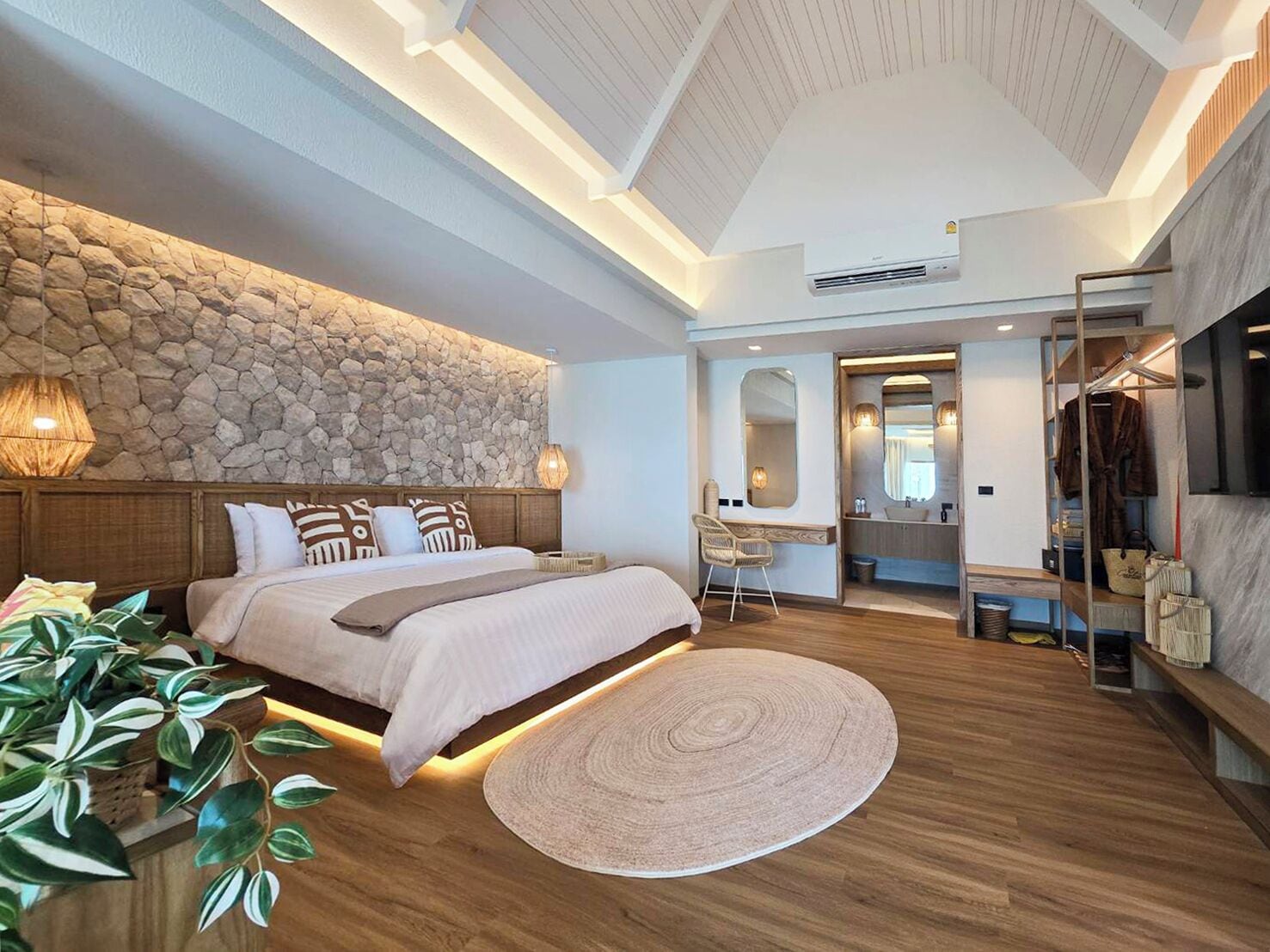 Une chambre moderne avec un mur en pierre, un lit en bois, un tapis rond et une salle de bain avec un miroir et un lavabo.