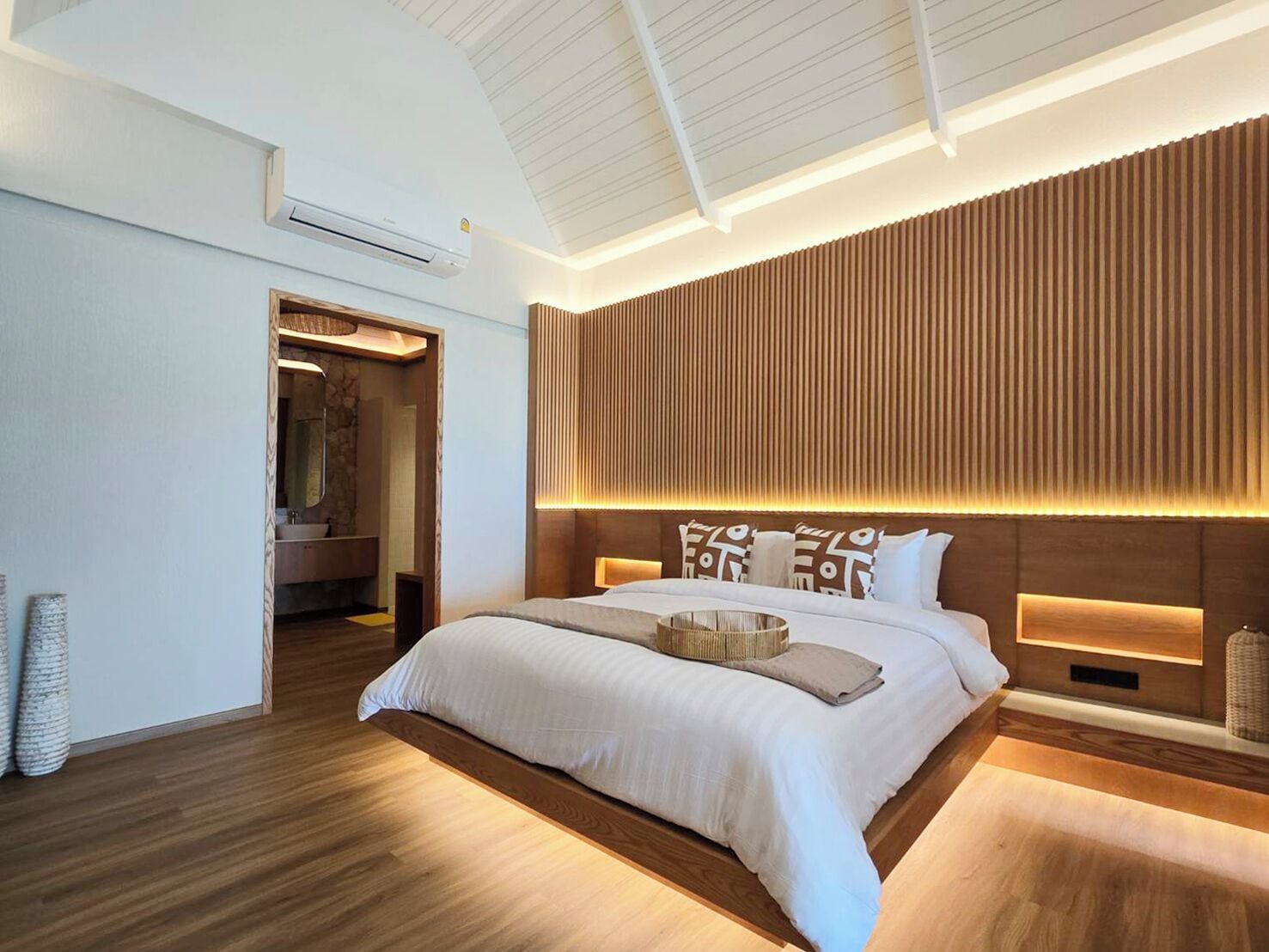Un dormitorio moderno con una cama grande, panel de pared de madera e iluminación integrada.