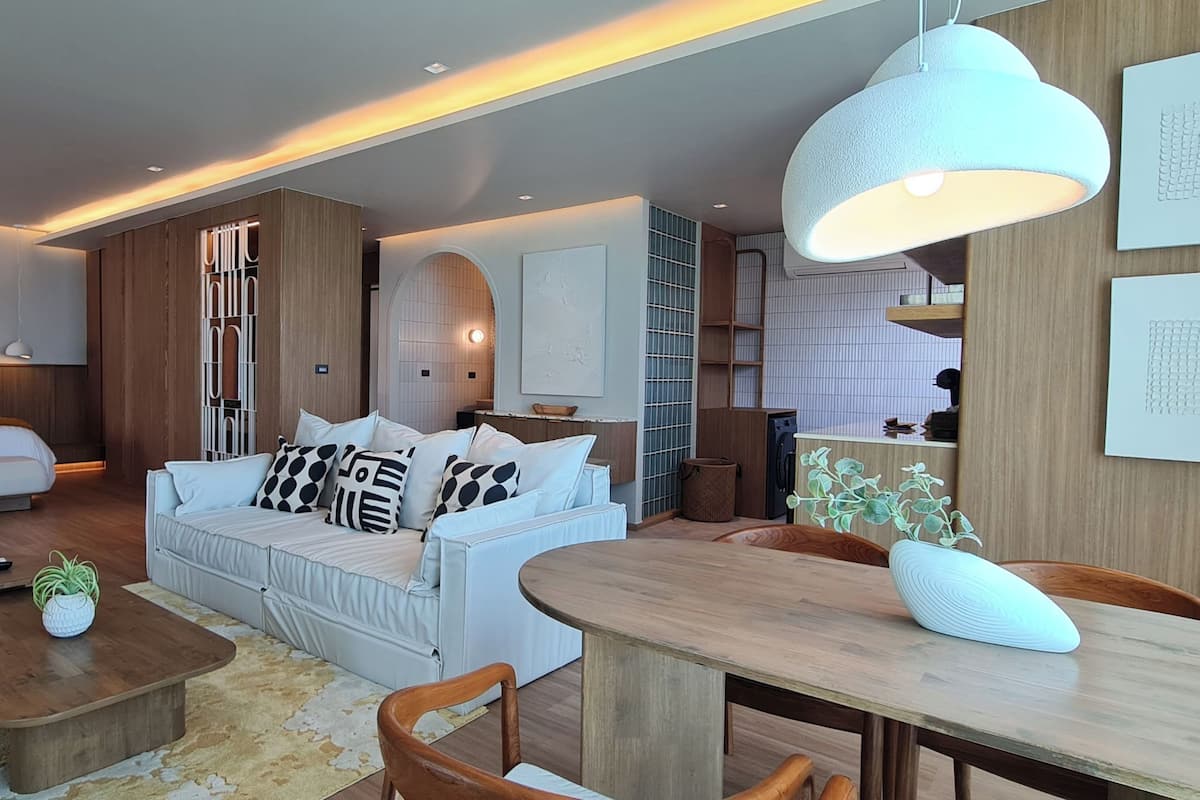 A modern hotel room with a large bed, a sofa, a dining table, and a kitchen area.