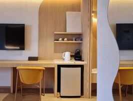 Una habitación de hotel compacta con kitchenette, un refrigerador pequeño, cafetera y dos sillas amarillas.