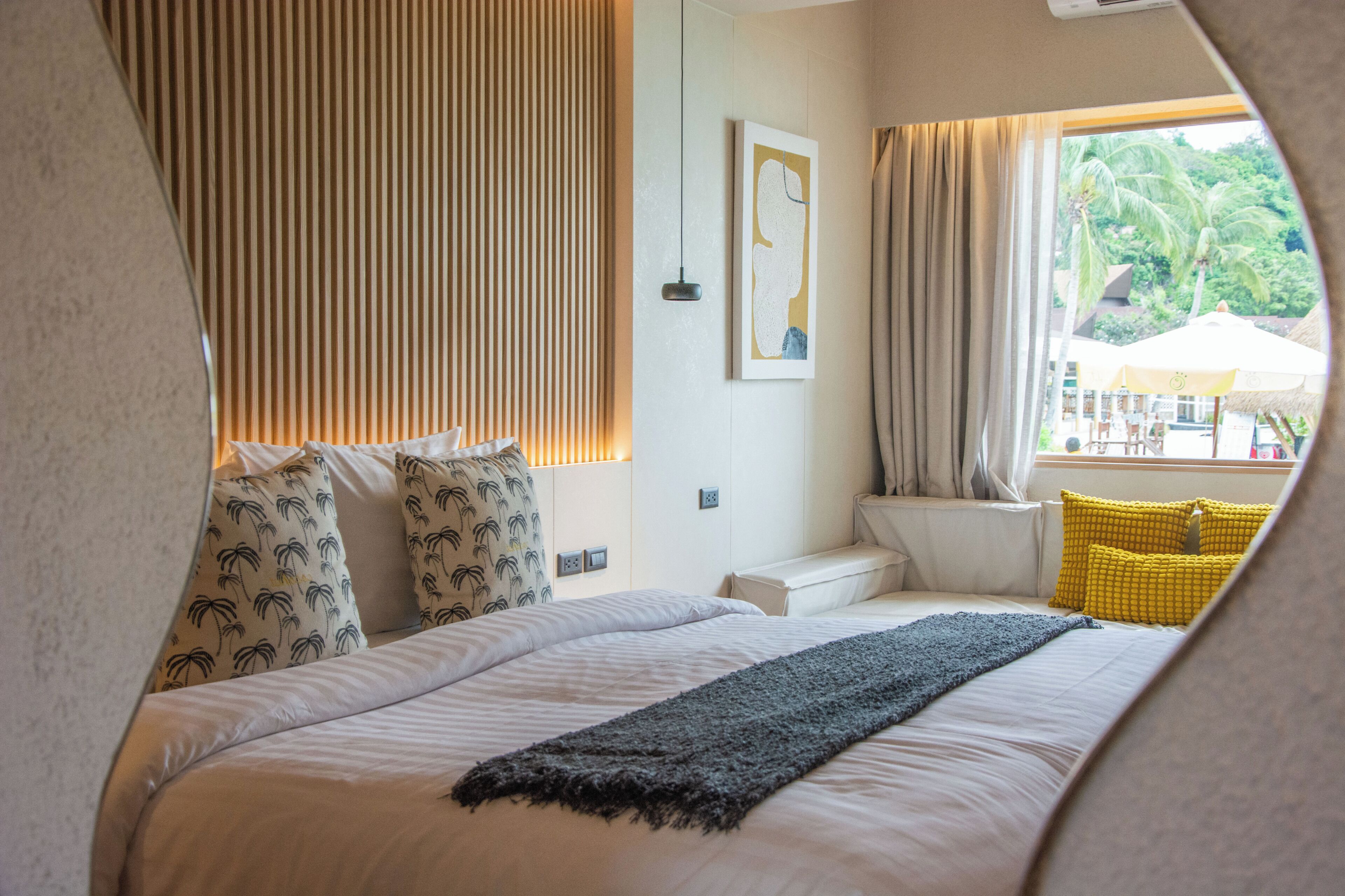 A bedroom with a bed, pillows, a blanket, a window with curtains, a wall-mounted light, and a framed picture.
