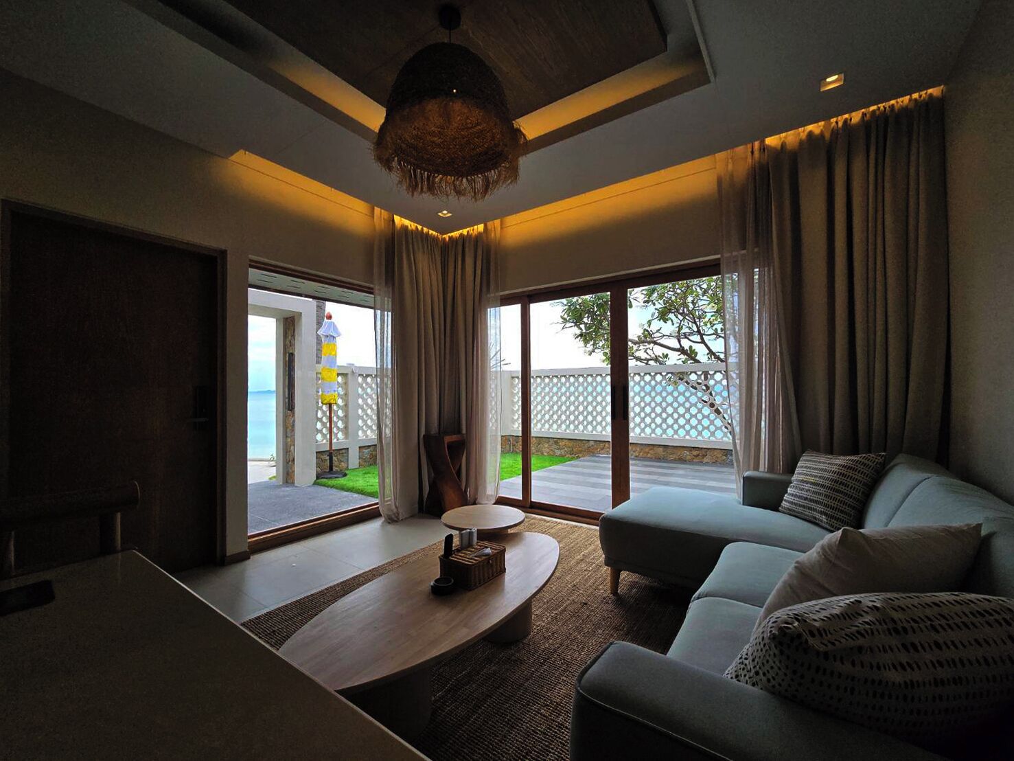 A modern living room with a sofa, coffee table, and a view of a deck and water.