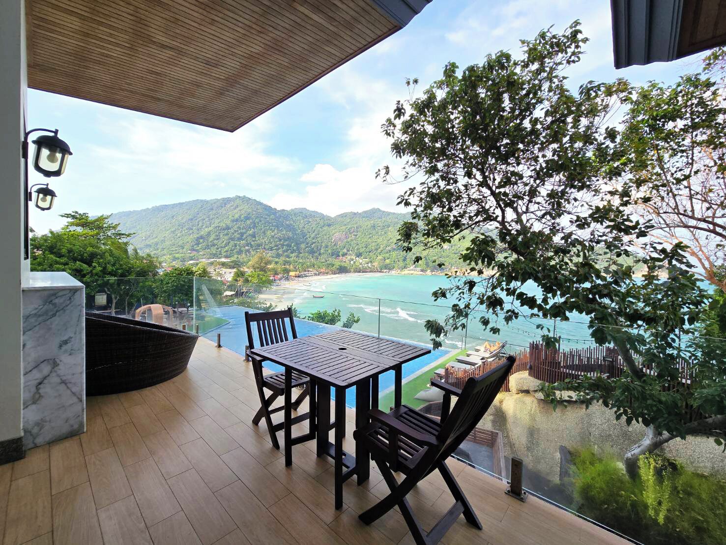 A terrace with a table and chairs overlooking a coastal view with mountains in the background.