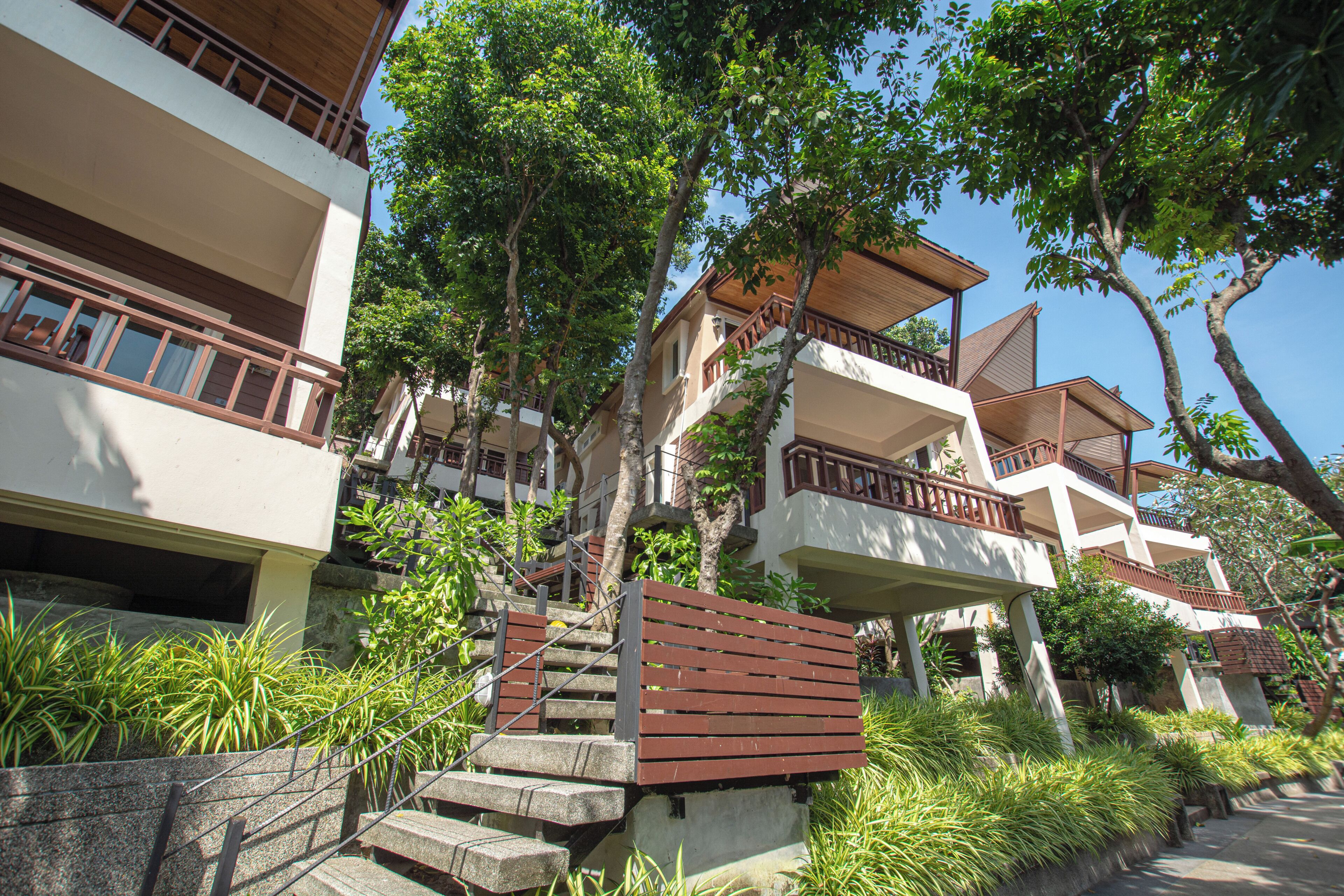 A multi-story building with balconies, a staircase, and surrounding greenery.